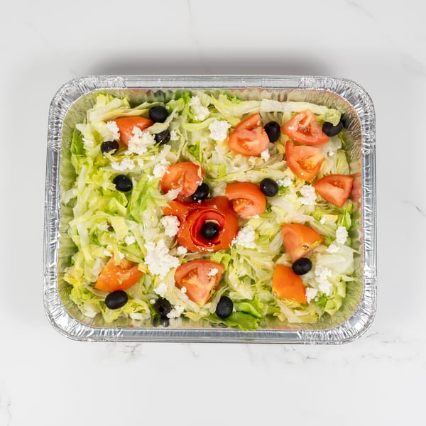 A large aluminum tray filled with a fresh salad of lettuce, tomatoes, black olives, and feta cheese.