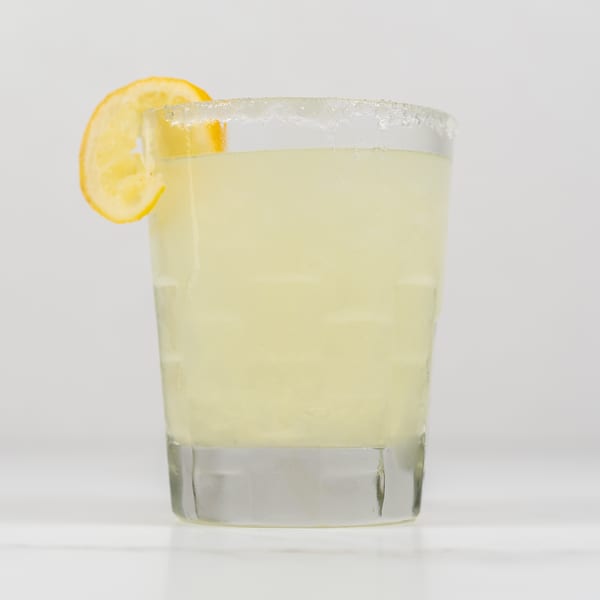 A glass of lemonade with a sugared rim and a lemon slice on a white background.