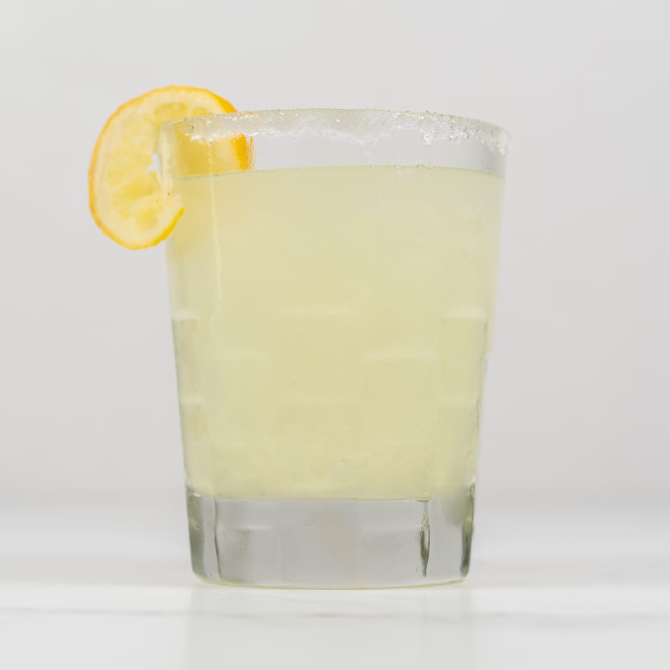 A glass of lemonade with a sugared rim and a lemon slice on a white background.