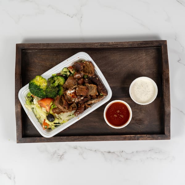 A takeout container with meat, broccoli, and salad, plus two sauce cups on a wooden tray.