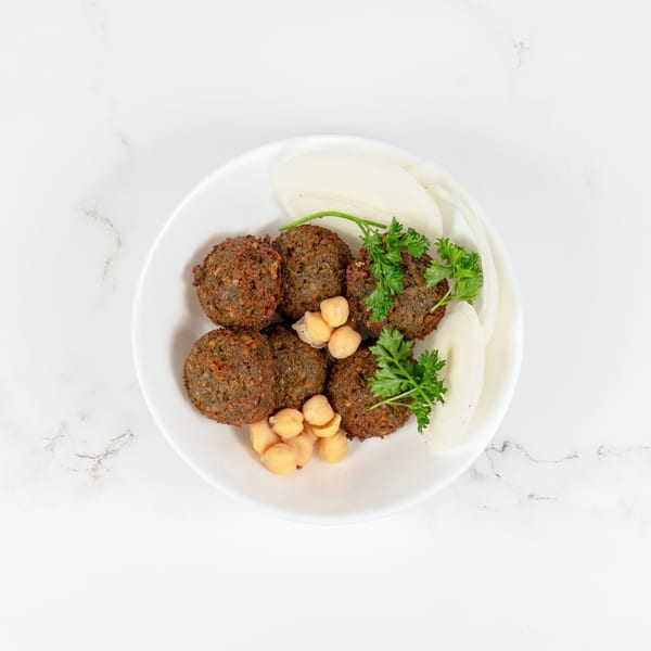 A white bowl filled with falafel, chickpeas, parsley, and sliced onions on a marble surface.