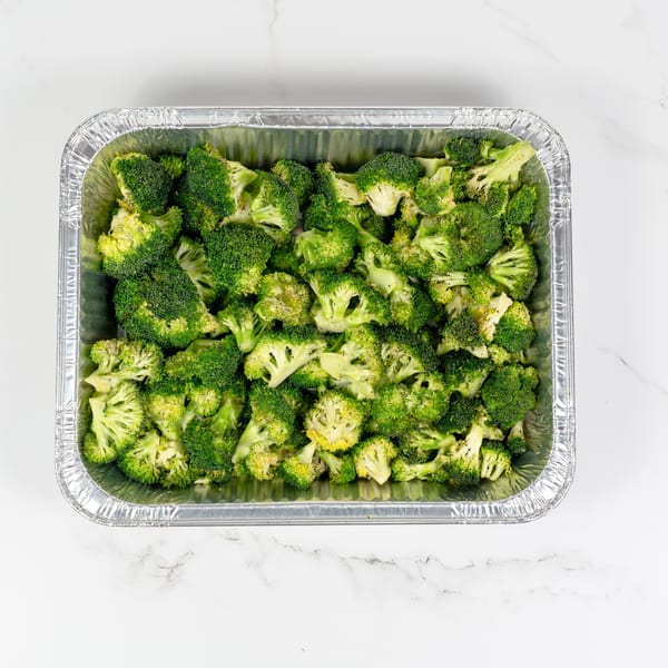 Fresh green broccoli florets, seasoned and ready for cooking, in a silver foil baking pan.