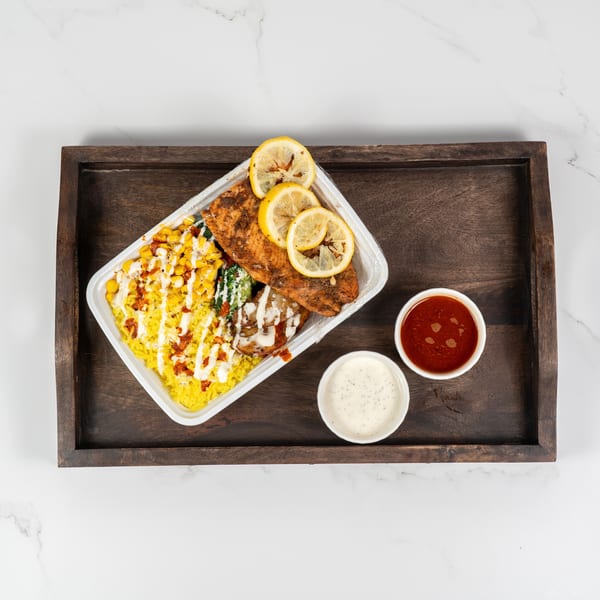 Grilled salmon with lemon slices, yellow rice, corn, and broccoli, with two dipping sauces on a wooden tray.