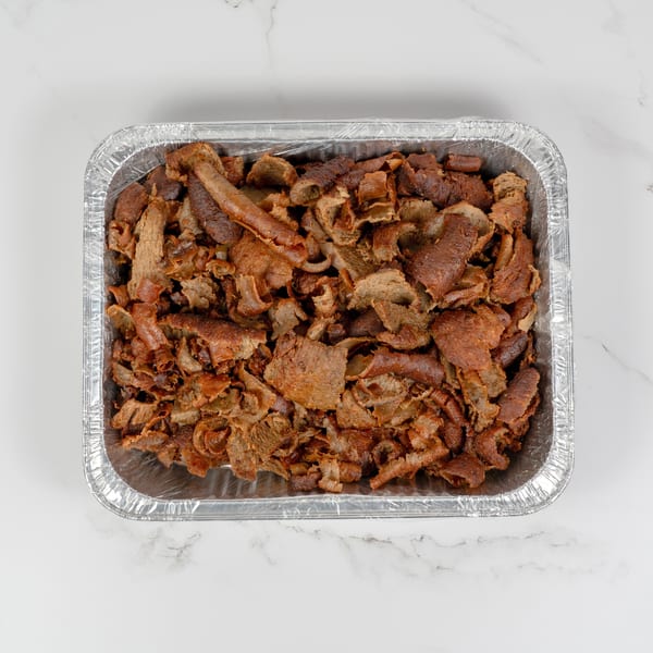 A foil tray filled with thinly sliced, browned gyro meat on a white marble surface.
