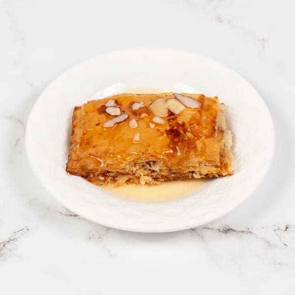 A golden-brown baklava pastry, drizzled with honey and topped with sliced almonds, on a white plate.