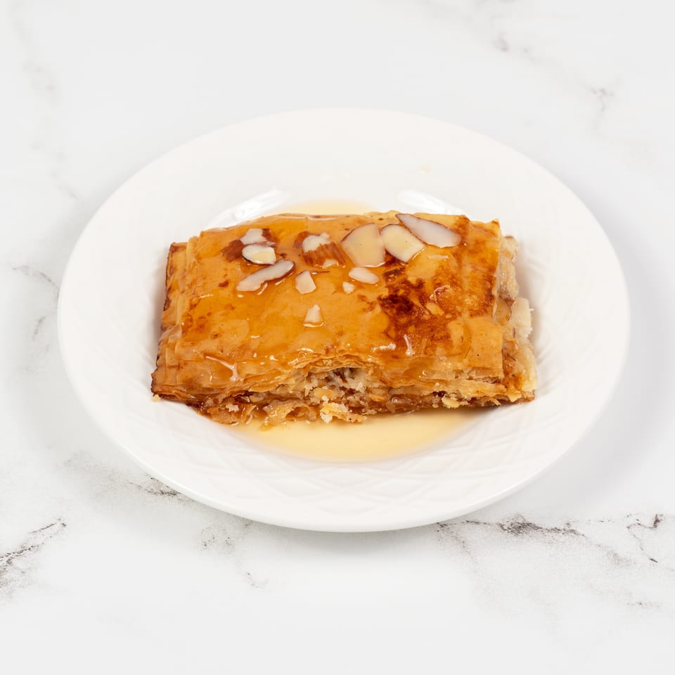 A golden-brown baklava pastry, drizzled with honey and topped with sliced almonds, on a white plate.