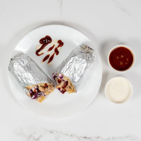 Two foil-wrapped burritos with visible fillings of chicken, red cabbage, and pineapple, served with sauces.