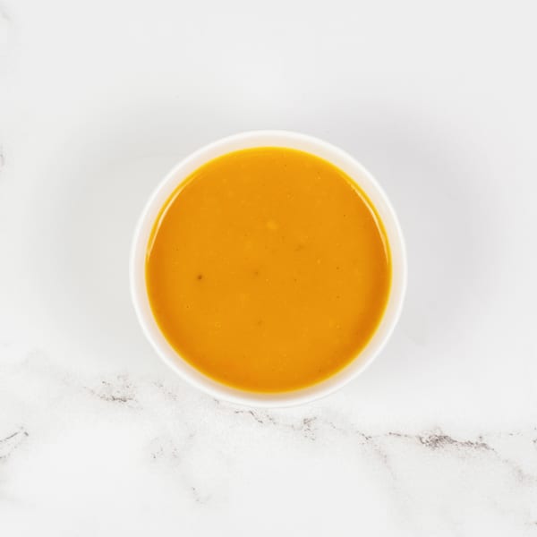 Overhead view of a white bowl filled with vibrant orange soup on a white marble surface.