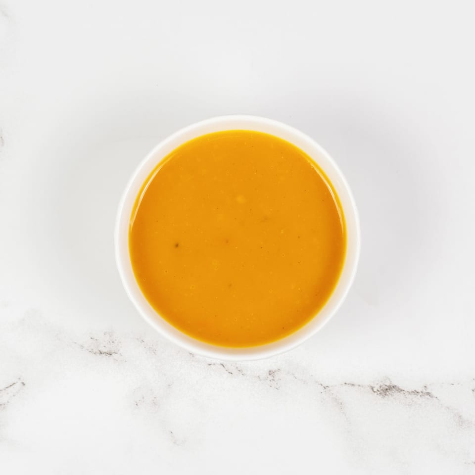 Overhead view of a white bowl filled with vibrant orange soup on a white marble surface.