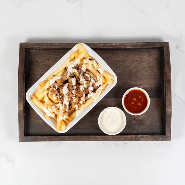Fries topped with chicken and white sauce, with two dipping sauces on a wooden tray.