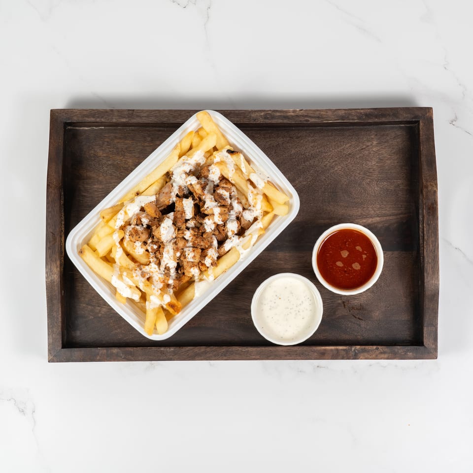 Fries topped with chicken and white sauce, with two dipping sauces on a wooden tray.