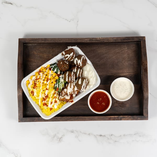 Falafel rice bowl with corn, broccoli, and sauces on a wooden tray.