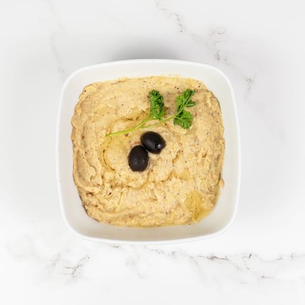Creamy hummus in a white bowl, garnished with two black olives, parsley, and olive oil.
